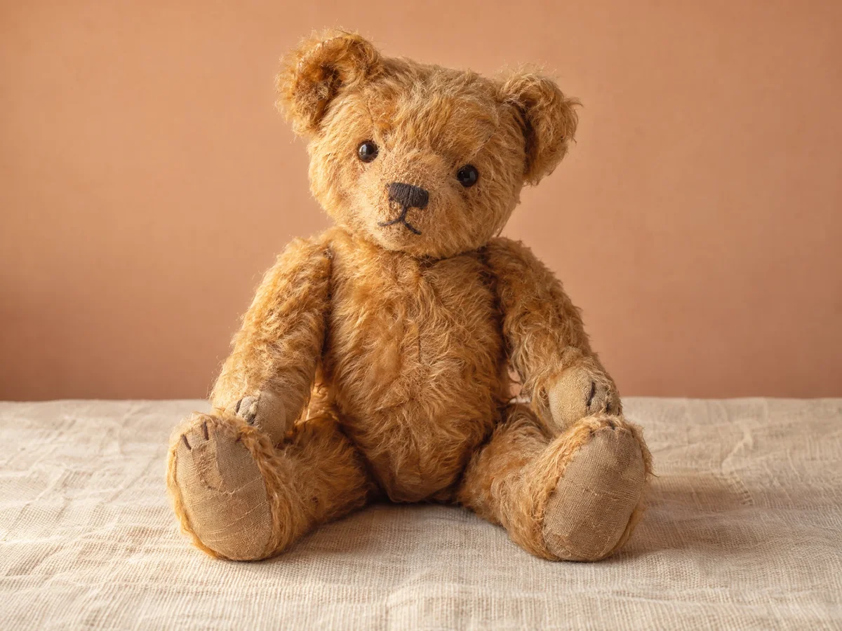 A honey-brown vintage-style teddy bear seated on a cream surface